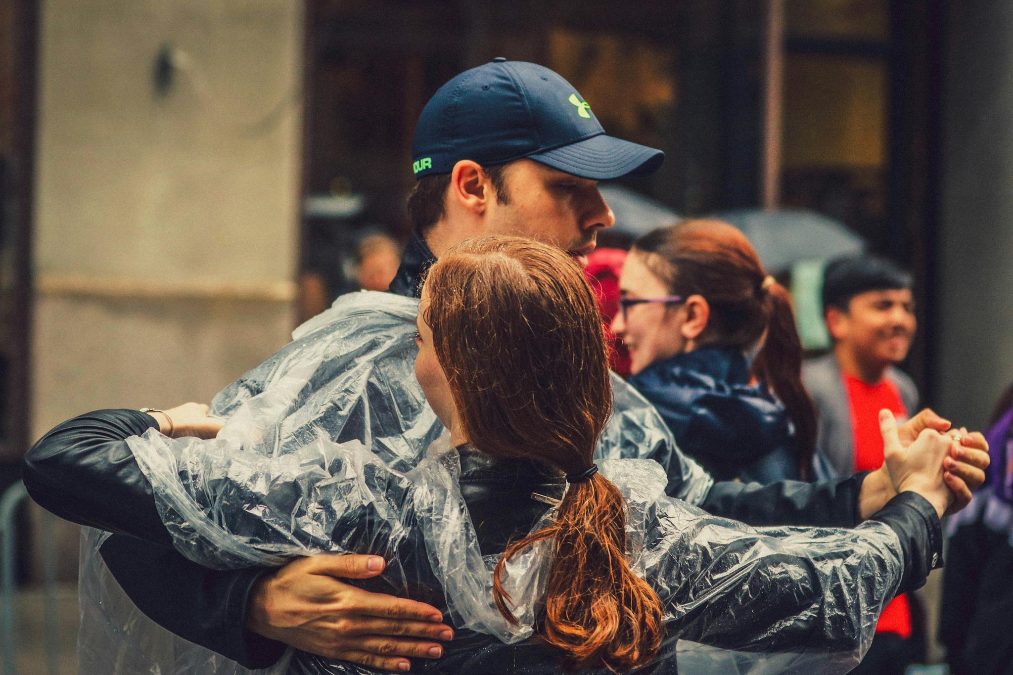 A couple in rain ponchos dancing passionately amidst a bustling New York street scene.