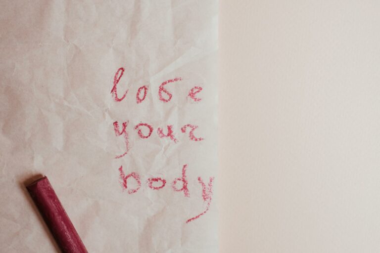 An inspiring 'love your body' message written on textured paper with red pastel crayon.